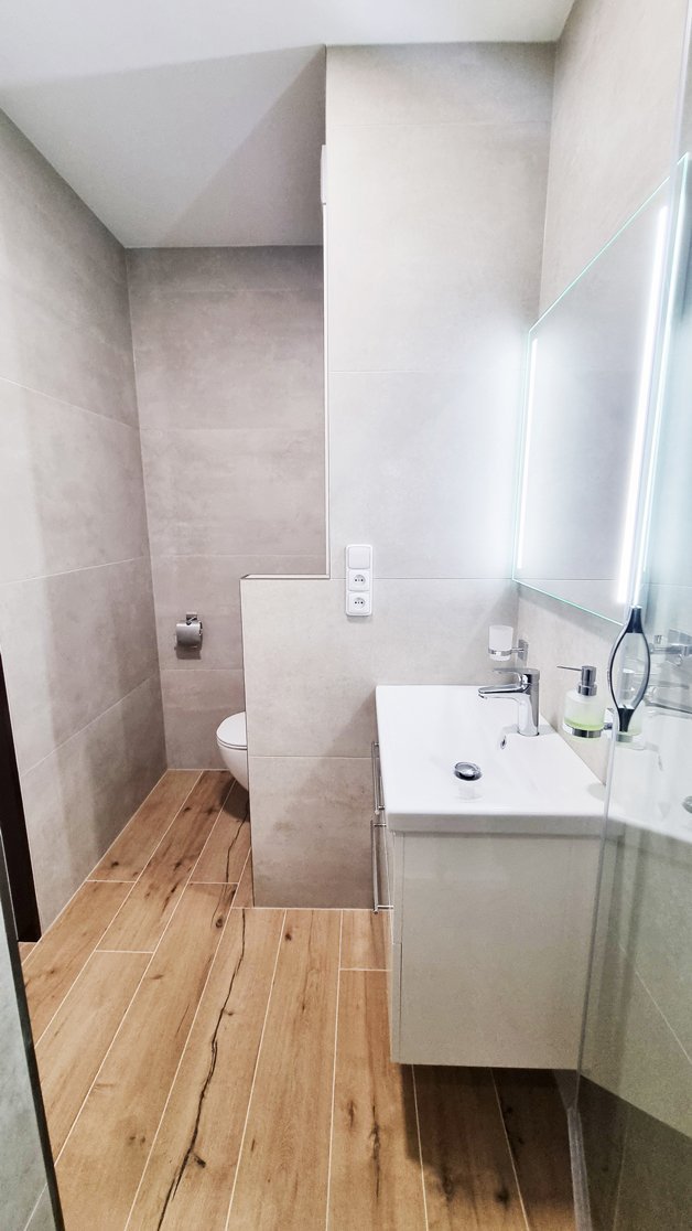 Celkový pohled na koupelnu s kombinací béžového velkoformátového obkladu a dlažby v dekoru dřeva Woodtale Miele. Rekonstrukce koupelny, kuchyně a interiéru bytu Svitavy, Hradec Králové | Pemtrade.cz