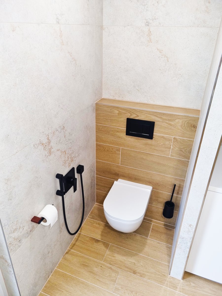Detail WC niky se závěsnou toaletou, obkladem v dekoru dřeva a černými doplňky. Rekonstrukce koupelny a interiéru bytu Svitavy, Hradec Králové | Pemtrade.cz