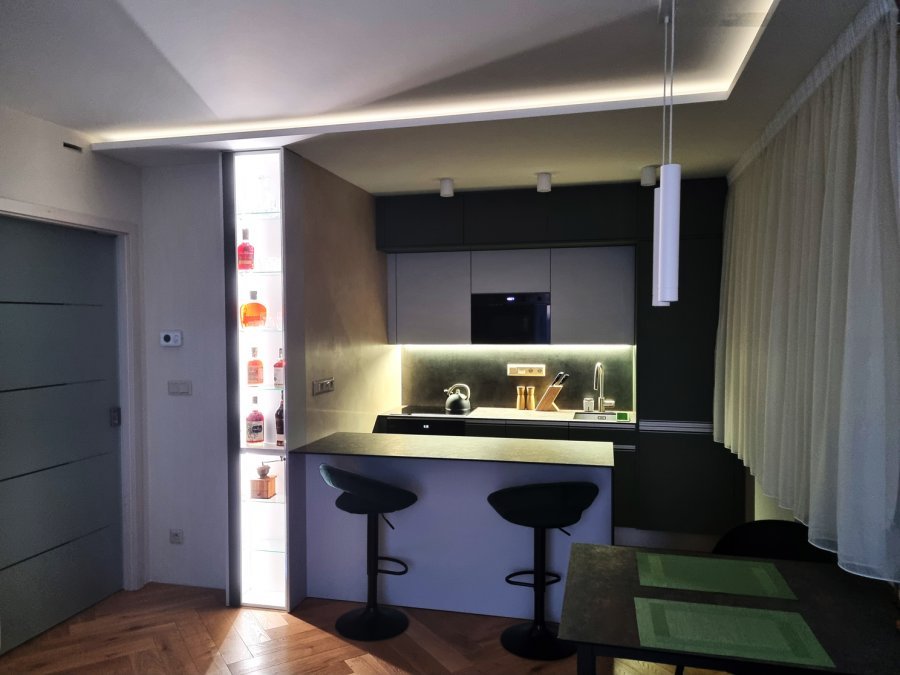 Večerní atmosféra kuchyně s podsvícenou pracovní zónou, barovým pultem a osvětlenou prosklenou nikou | Realizace kuchyně a interiéru byt Svitavy, Hradec Králové | Pemtrade.cz